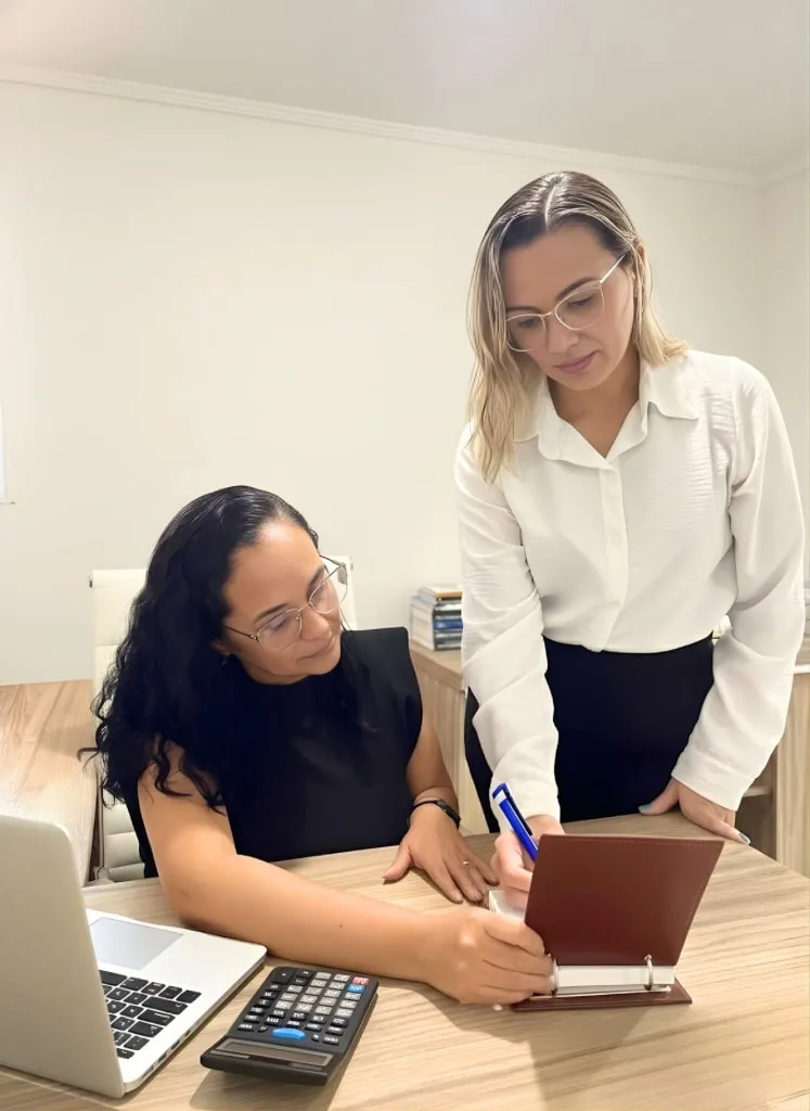 Duas profissionais da Contae Contabilidade revisam documentos à mesa do escritório